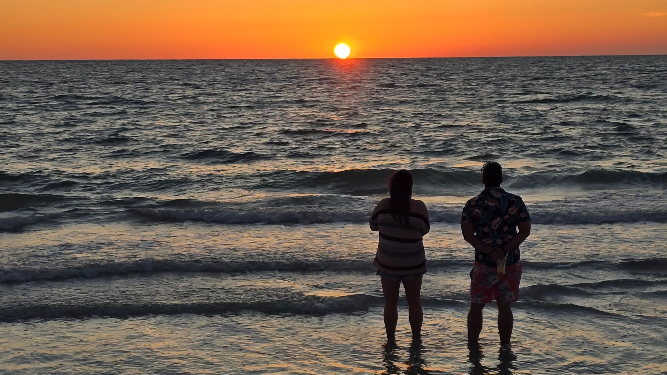 Beach sunset with two people standing by the shoreline